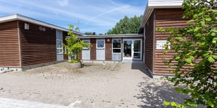 Indgangspartiet til daginstitutionen Rumlepotten i Næstved Kommune. Husets facader er i træ og består af to huse, der er sammenbygget med et vindfang.