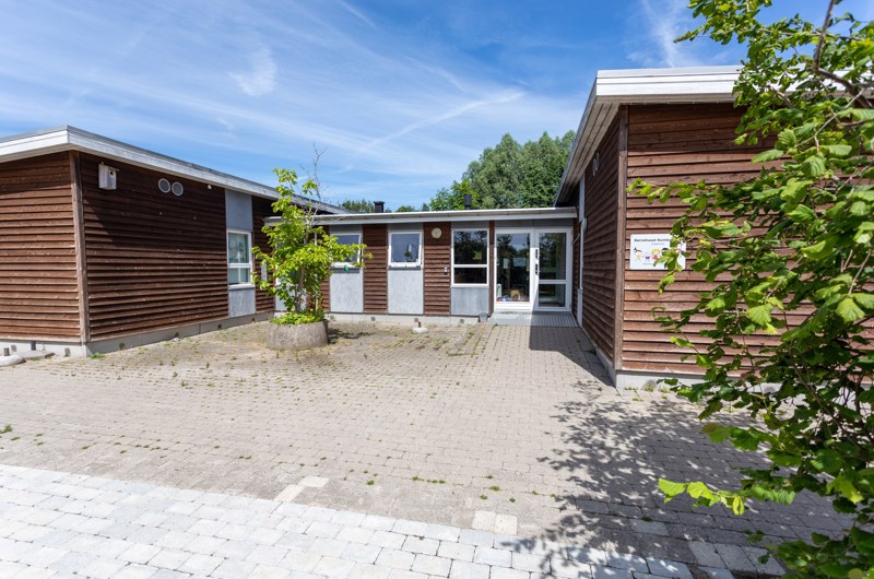 Indgangspartiet til daginstitutionen Rumlepotten i Næstved Kommune. Husets facader er i træ og består af to huse, der er sammenbygget med et vindfang.