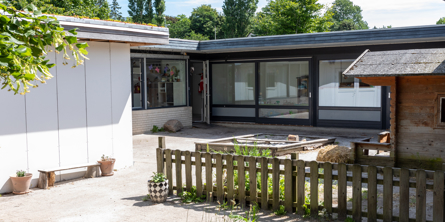 Gård med sandkasse til de mindste børn, hvis bygning og store vinduer set fra bagsiden af Børnehjørnet.