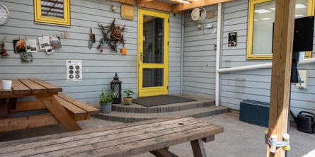 Indgangspartiet til daginstitutionen Skattekisten i Næstved Kommune. Husets facader er i lyseblåt træ, med gule vinduer. Indgangen er overdækket.