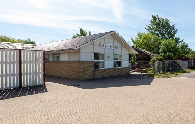 Indgangspartiet til daginstitutionen Birkehegnet i Næstved Kommune. Husets facader er en blanding af gule mursten og hvide plader. Der vokser træer bag bygningen.