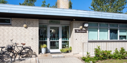 Indgangspartiet til daginstitutionen Skovtrolden i Næstved Kommune. Bygningen er i  hvide sten. Der er cykelparkering foran huset.