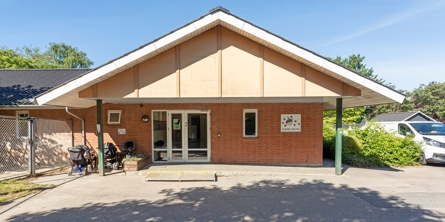 Indgangspartiet til daginstitutionen Kornblomsten i Næstved Kommune. Huset er i røde mursten og ligger direkte ud til parkeringspladsen.