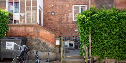 Indgang til Mariehuset med trappe op til hoveddøren til ældre hus med røde mursten. Et par børnecykler i forgrunden.