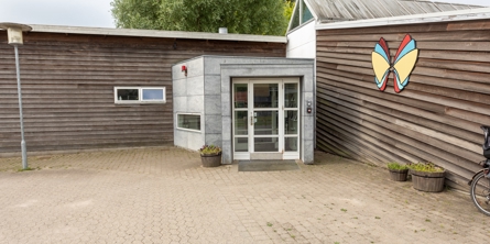 Indgangspartiet til daginstitutionen Sommerfugl i Næstved Kommune. Husets facader er i træ og indgangen er i metal og glas. 