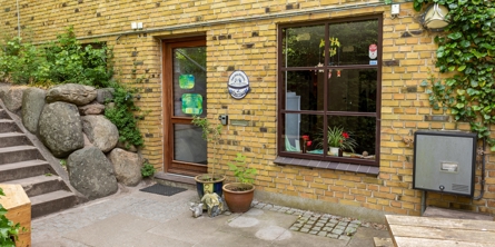 Indgangspartiet til daginstitutionen Egernbo i Næstved Kommune. Bygningen er opført i gule melerede sten. Foran er der stensætning og en mindre trappe. 