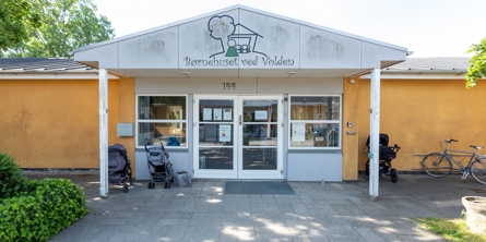 Indgangspartiet til daginstitutionen Volden i Næstved Kommune. Husets facade er gul. Indgangen er overdækket og der er vinduer og døre i glas. 