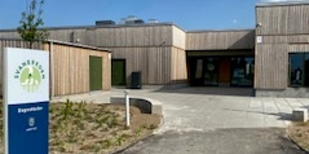 Billede af Svaneredens indgangsparti, der viser skilt med daginstitutionens navn, den brune nybyggede bygning og hovedindgangen