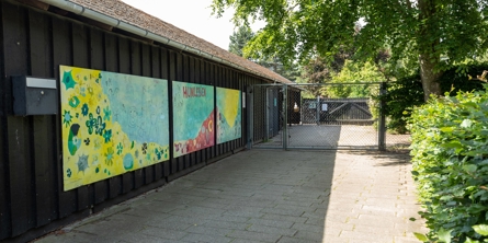 Indgangspartiet til daginstitutionen Humlebien i Næstved Kommune. Husets facader er i  sort træ. Der er opsat tre store malerier på bygningens side. 