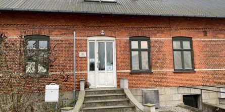 Indgang til Bølgen, ældre hus af røde mursten med trappe op til hoveddøren. der er også 3 vinduer + nedgang til kælder i højre side af billedet.